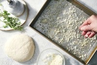 Grated Paremsan being sprinkled into an oiled pizza pan before adding the dough on top.